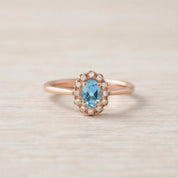 A rose gold ring with a blue gemstone set in the center, surrounded by small diamonds.
