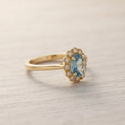 A gold ring with a blue gemstone, likely a diamond, set in the center of the band.