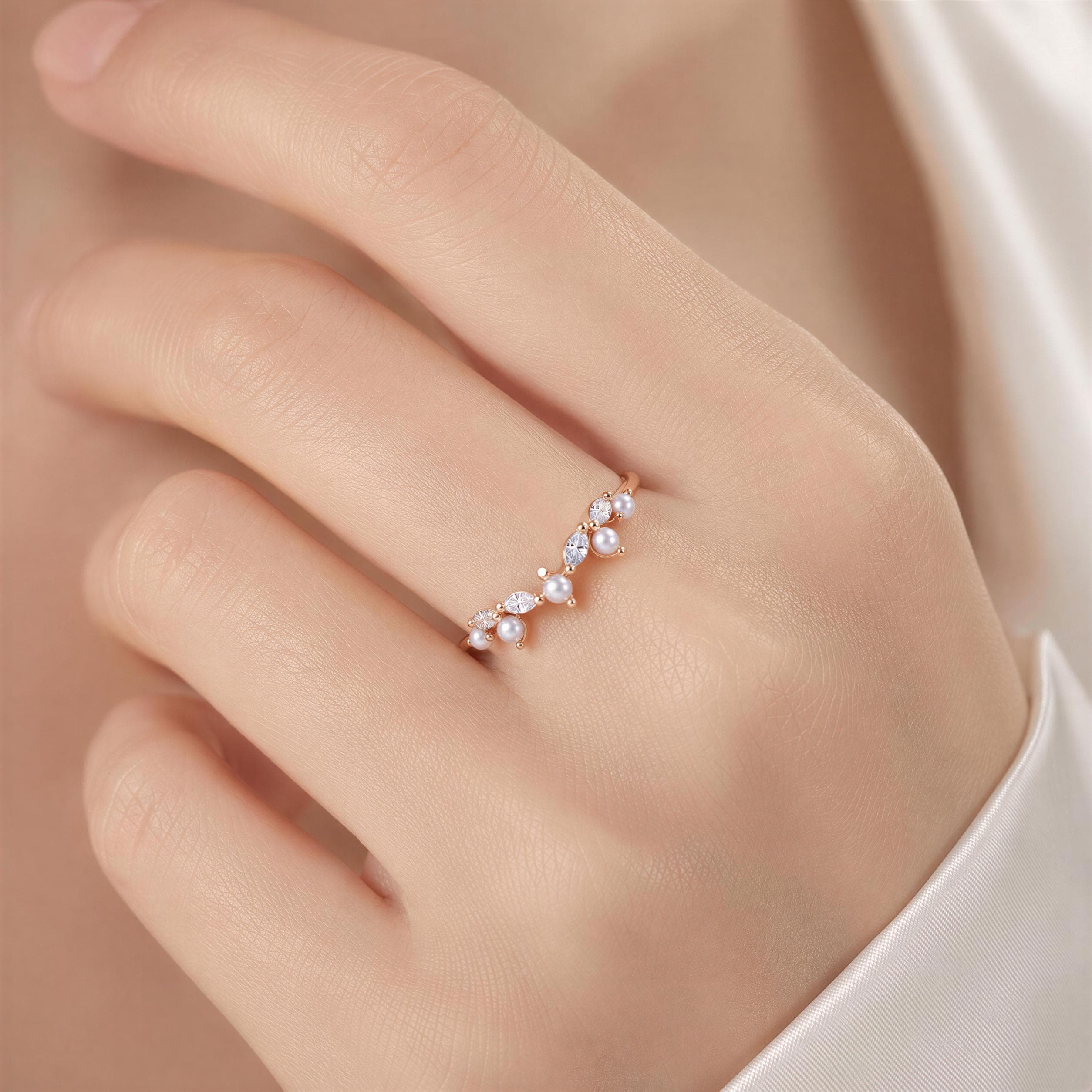 A close-up of a hand wearing a delicate gold ring with a cluster of small pearls and a small diamond.