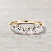 A gold ring with a decorative band and a row of pearls and diamonds set in it, resting on a wooden surface.