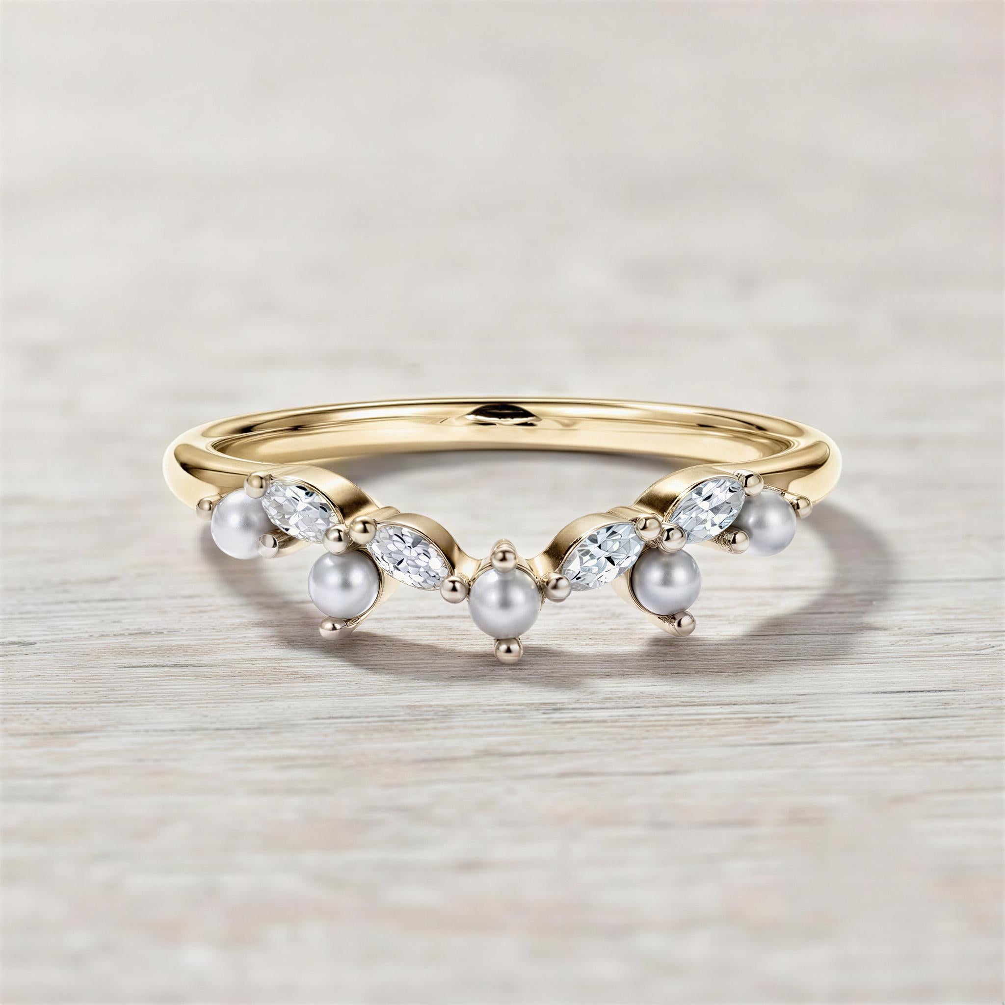 A gold ring with a decorative band and a row of pearls and diamonds set in it, resting on a wooden surface.
