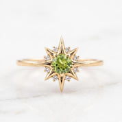 A gold ring with a large central green gemstone surrounded by smaller diamonds, resembling a starburst design.