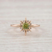 A gold ring with a large green gemstone in the center, surrounded by smaller diamonds, set against a light wooden background.