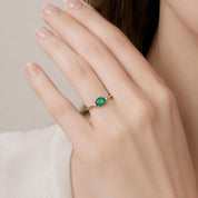 A close-up of a person's hand wearing a gold ring with a green gemstone.