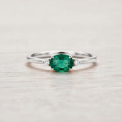 A silver ring with a large oval-shaped green gemstone in the center, surrounded by smaller diamonds.