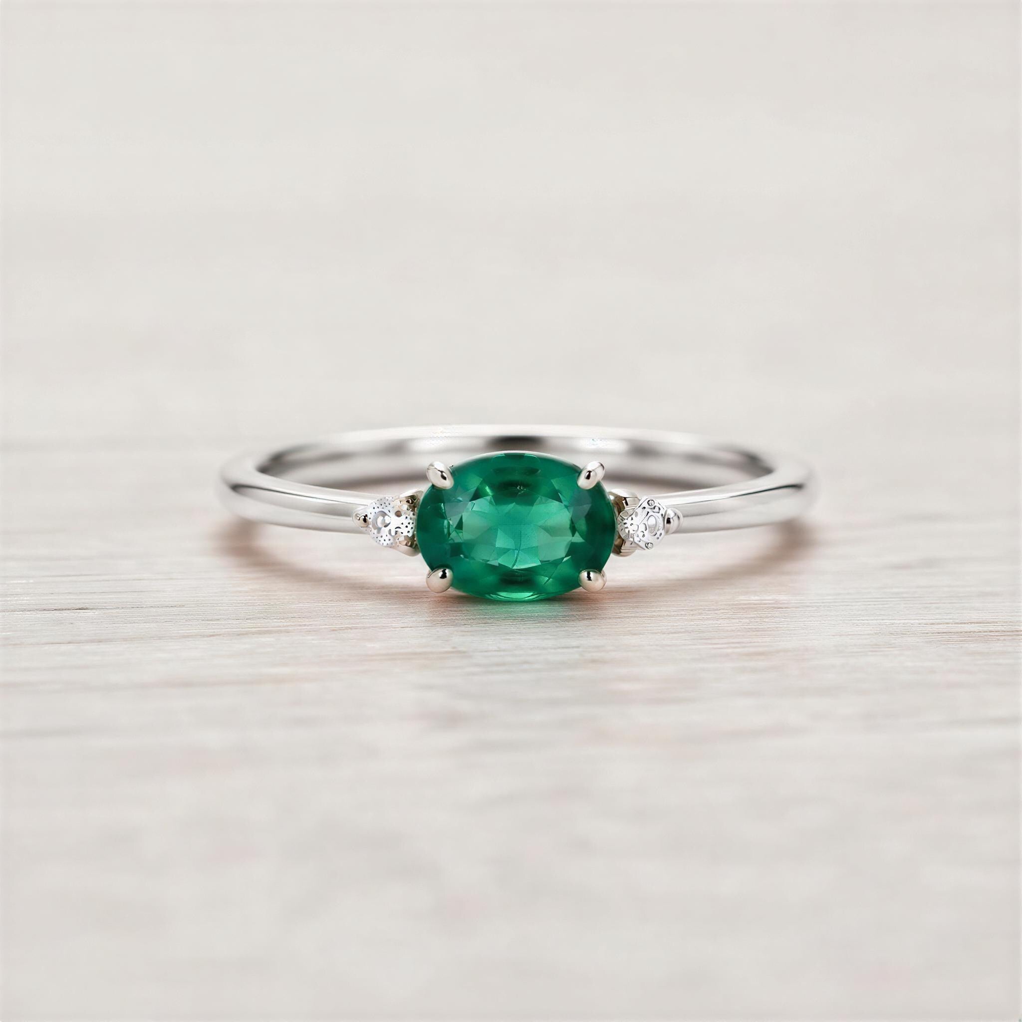 A silver ring with a large oval-shaped green gemstone in the center, surrounded by smaller diamonds.