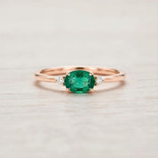 A rose gold ring with a large oval-shaped green gemstone, possibly an emerald, set in the center.