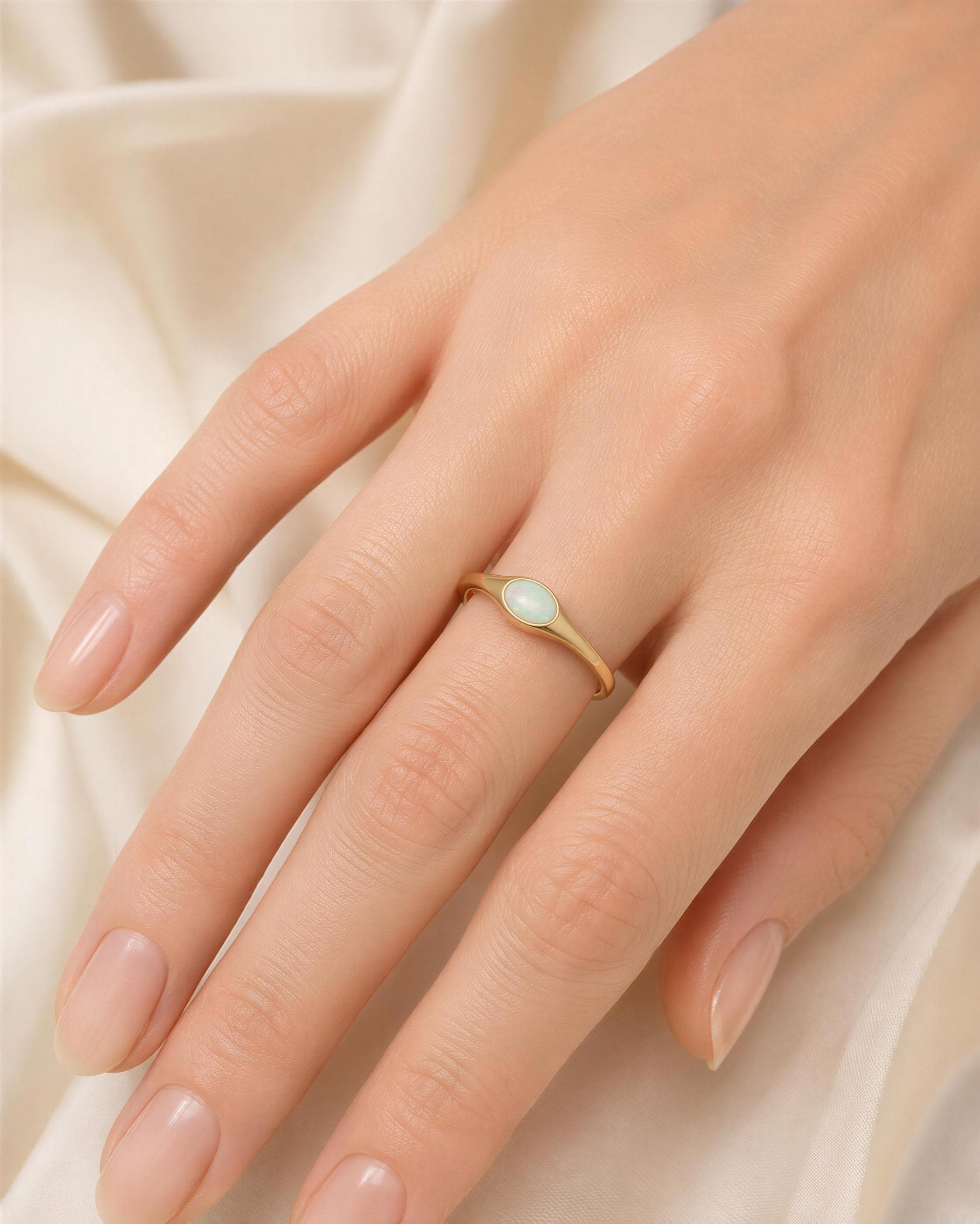 A close-up of a person's hand wearing a gold ring with a small, round opal stone.