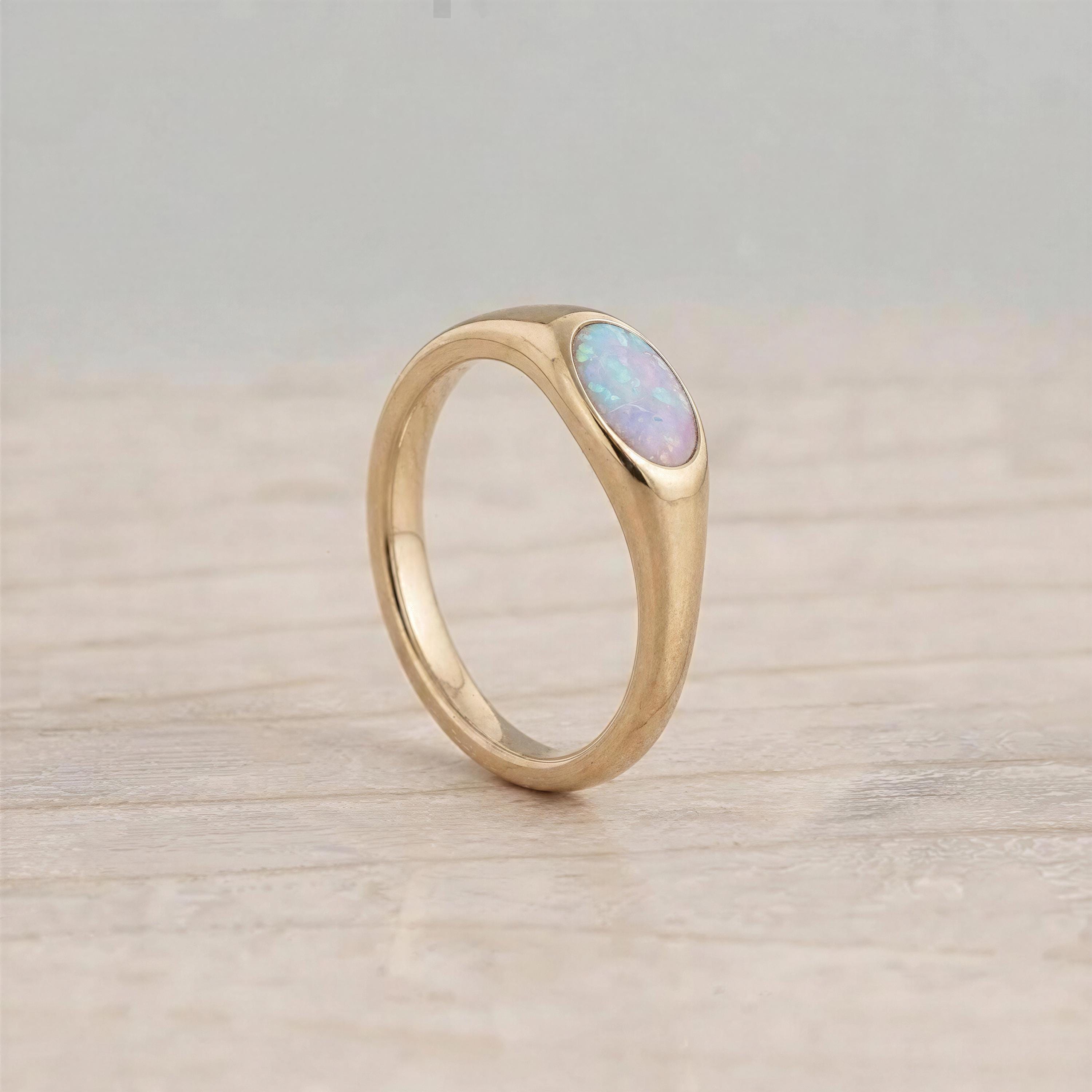 A gold ring with a large oval-shaped opal stone set in the center, resting on a wooden surface.