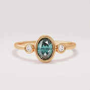 A gold ring with a large oval-shaped gemstone in the center, surrounded by smaller diamonds on either side.