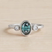 A silver ring with a large oval-shaped gemstone in the center, surrounded by smaller round stones.