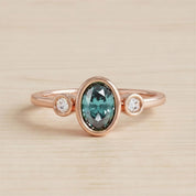 A rose gold ring with a large oval-shaped gemstone in the center, surrounded by smaller round stones.