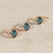 Three rings with gemstones are displayed on a wooden surface.