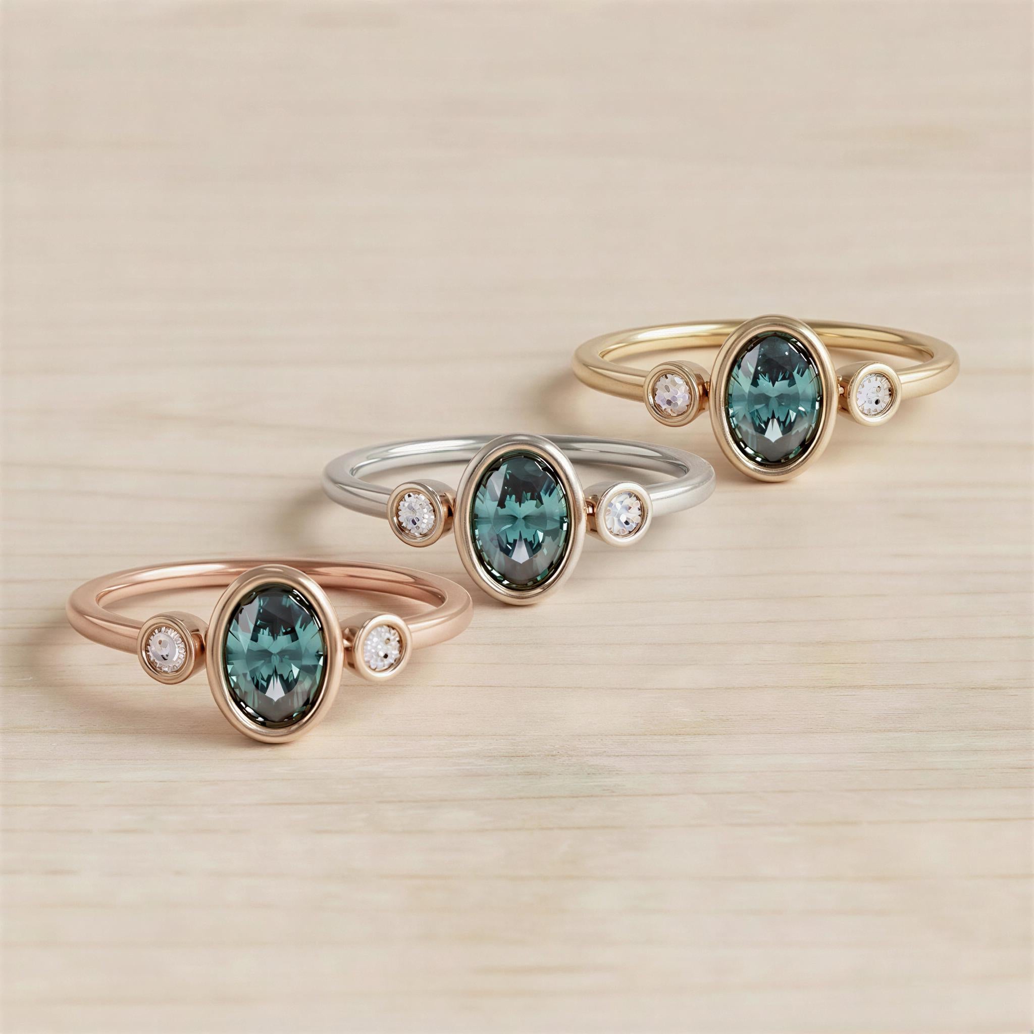 Three rings with gemstones are displayed on a wooden surface.