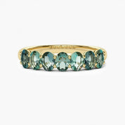 A gold ring with a row of green gemstones, likely tourmalines, set in the band.