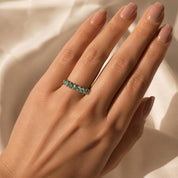 A close-up of a hand wearing a ring with a row of green gemstones.