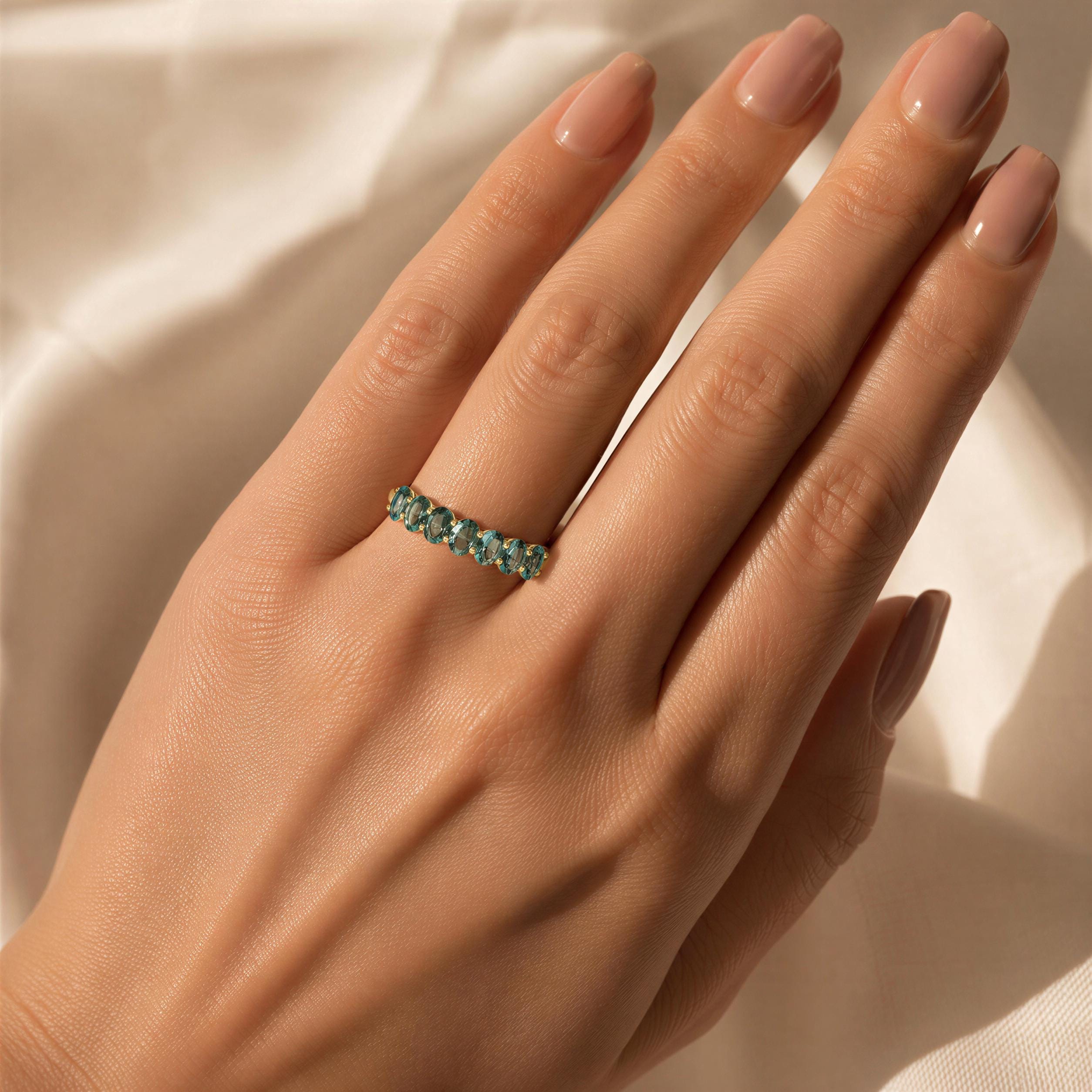 A close-up of a hand wearing a ring with a row of green gemstones.