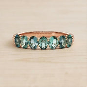 A gold ring with a row of green gemstones, likely tourmalines, set in the band.