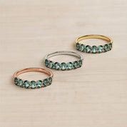 Three rings with green gemstones are displayed on a wooden surface.