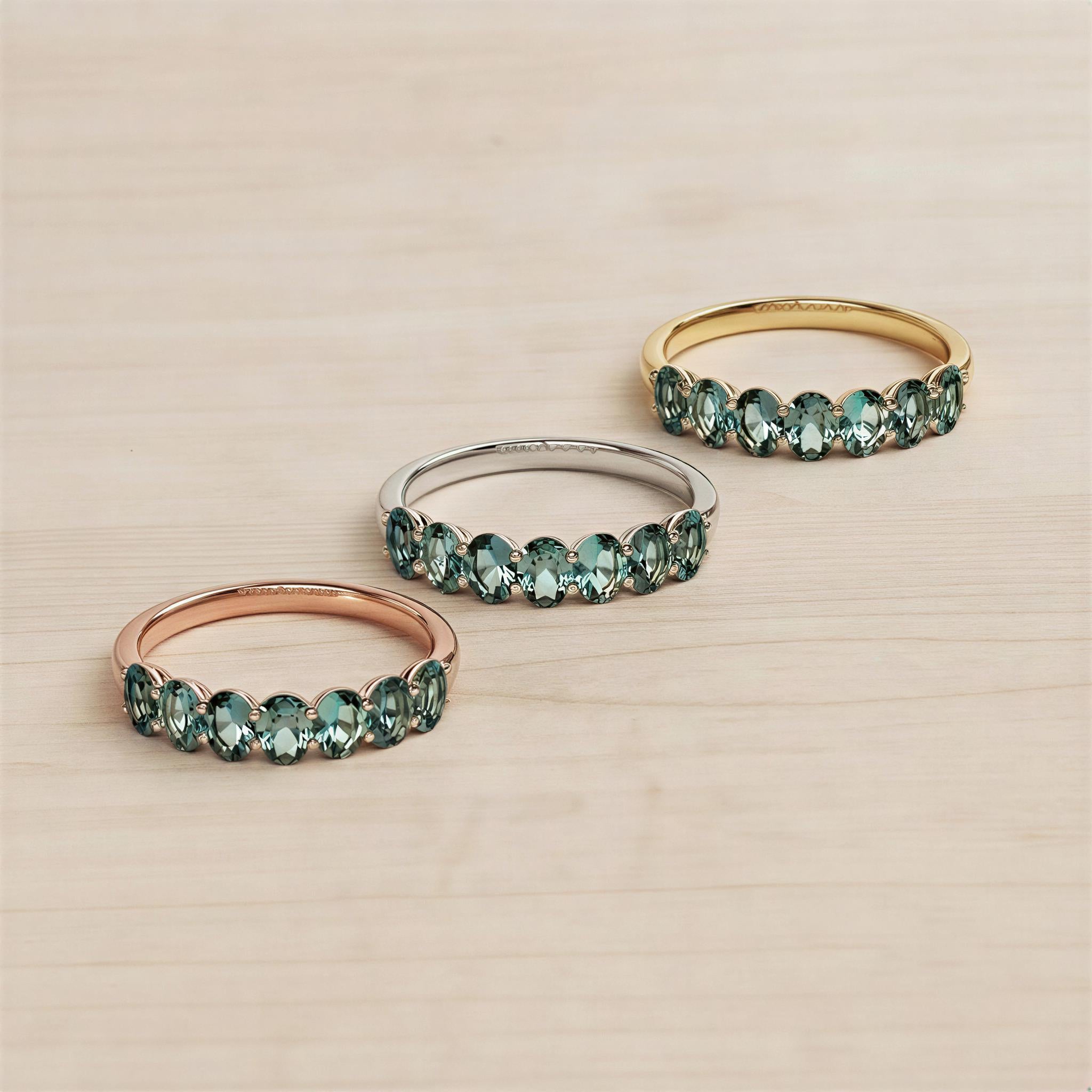Three rings with green gemstones are displayed on a wooden surface.