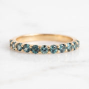 A gold band with a row of blue sapphires set in it, displayed on a white marble surface.