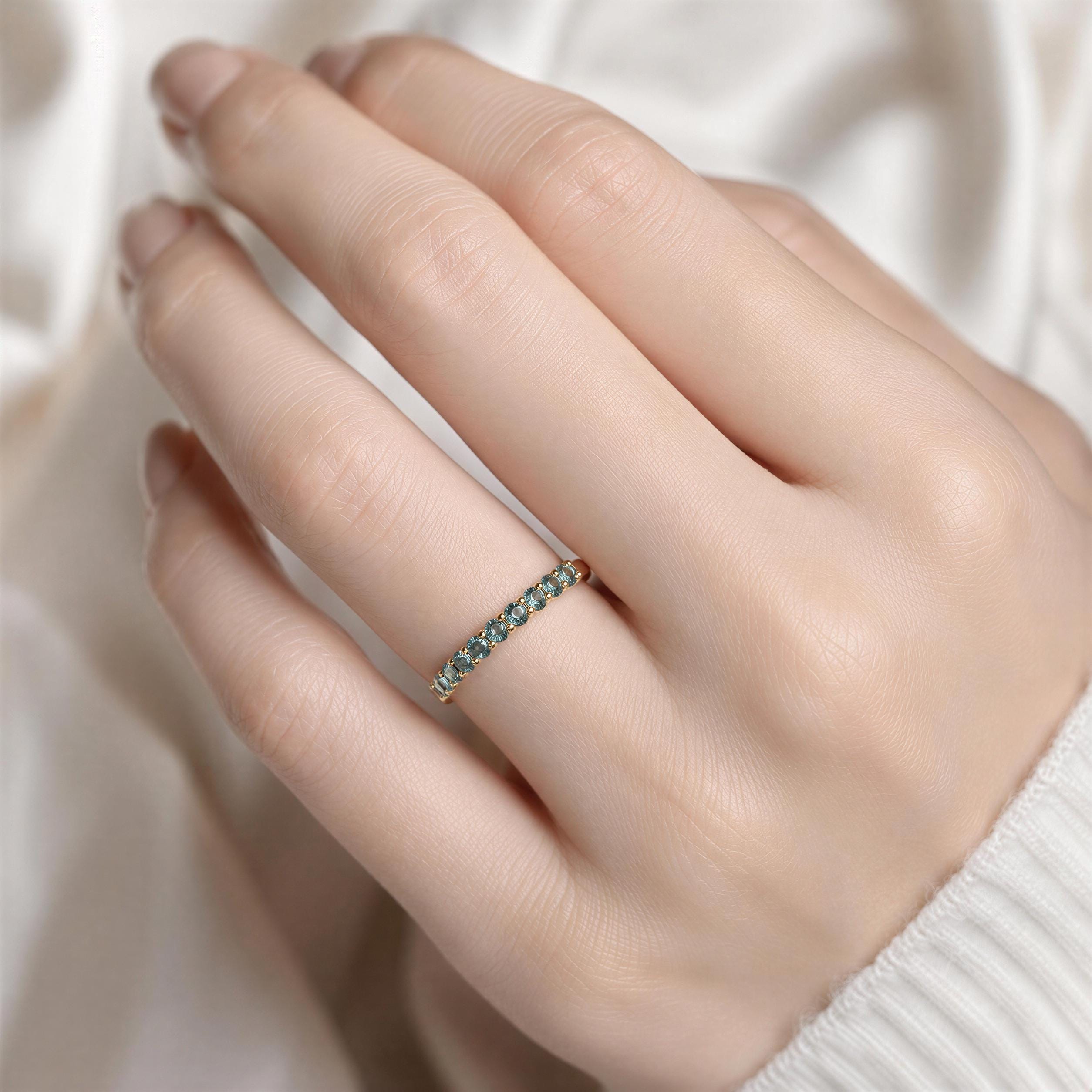 A close-up of a person's hand wearing a gold ring with a row of blue gemstones.