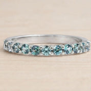 A silver ring with a row of blue gemstones, including turquoise and aquamarine stones, set in a band.