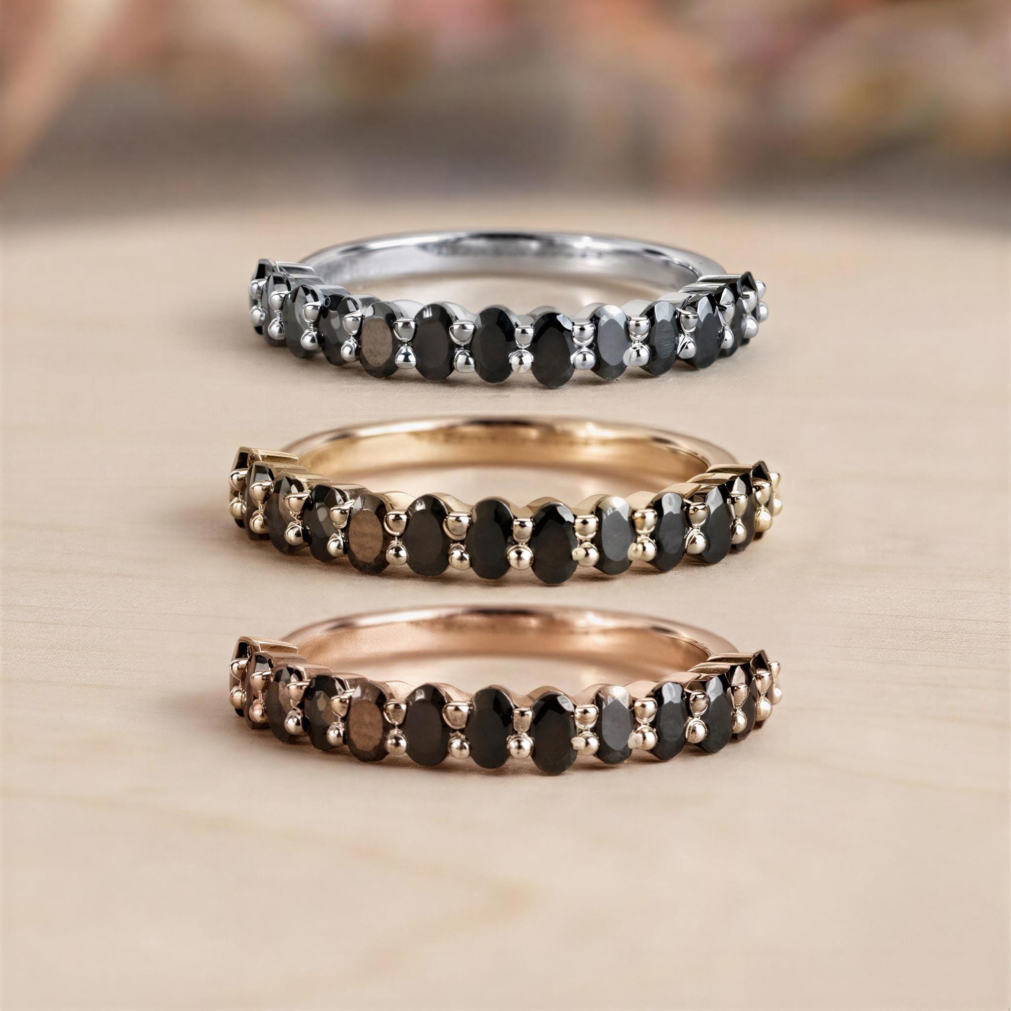 Three rings with black stones arranged in a row, each with a different color: silver, gold, and brown.