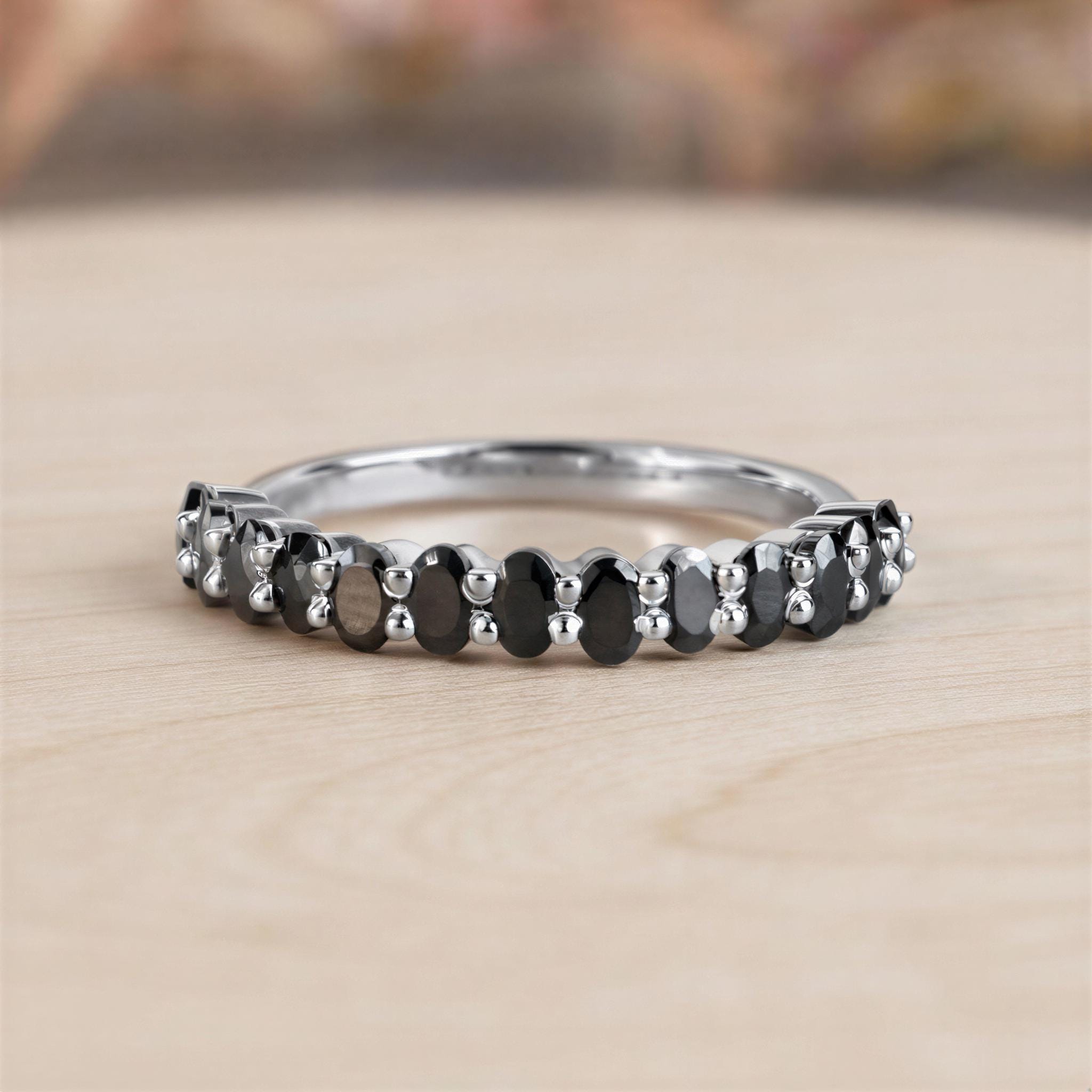 A silver ring with a row of black diamonds set in it, resting on a wooden surface.