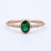 A gold ring with a large oval-shaped green gemstone set in the center, surrounded by smaller diamonds.