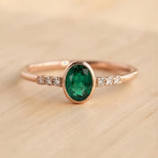 A gold ring with a large oval-shaped green gemstone, surrounded by smaller diamonds, resting on a wooden surface.