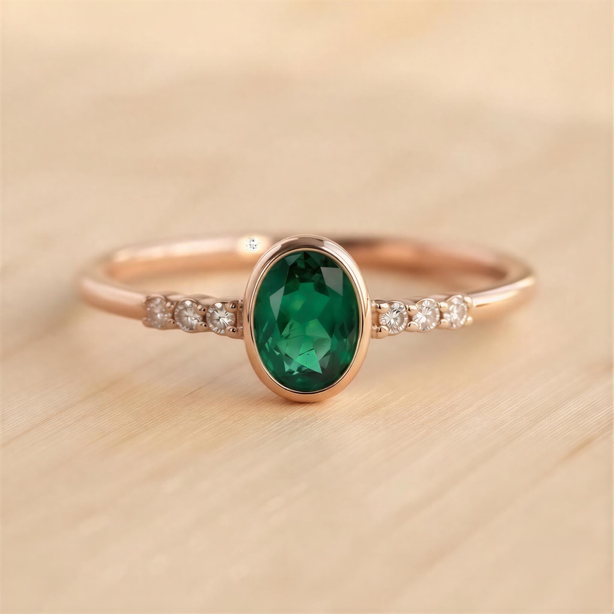 A gold ring with a large oval-shaped green gemstone, surrounded by smaller diamonds, resting on a wooden surface.