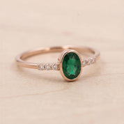 A gold ring with a large oval-shaped green gemstone, surrounded by smaller diamonds, resting on a light-colored surface.