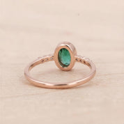 A rose gold ring with a large oval-shaped gemstone, likely an emerald, set in the center.