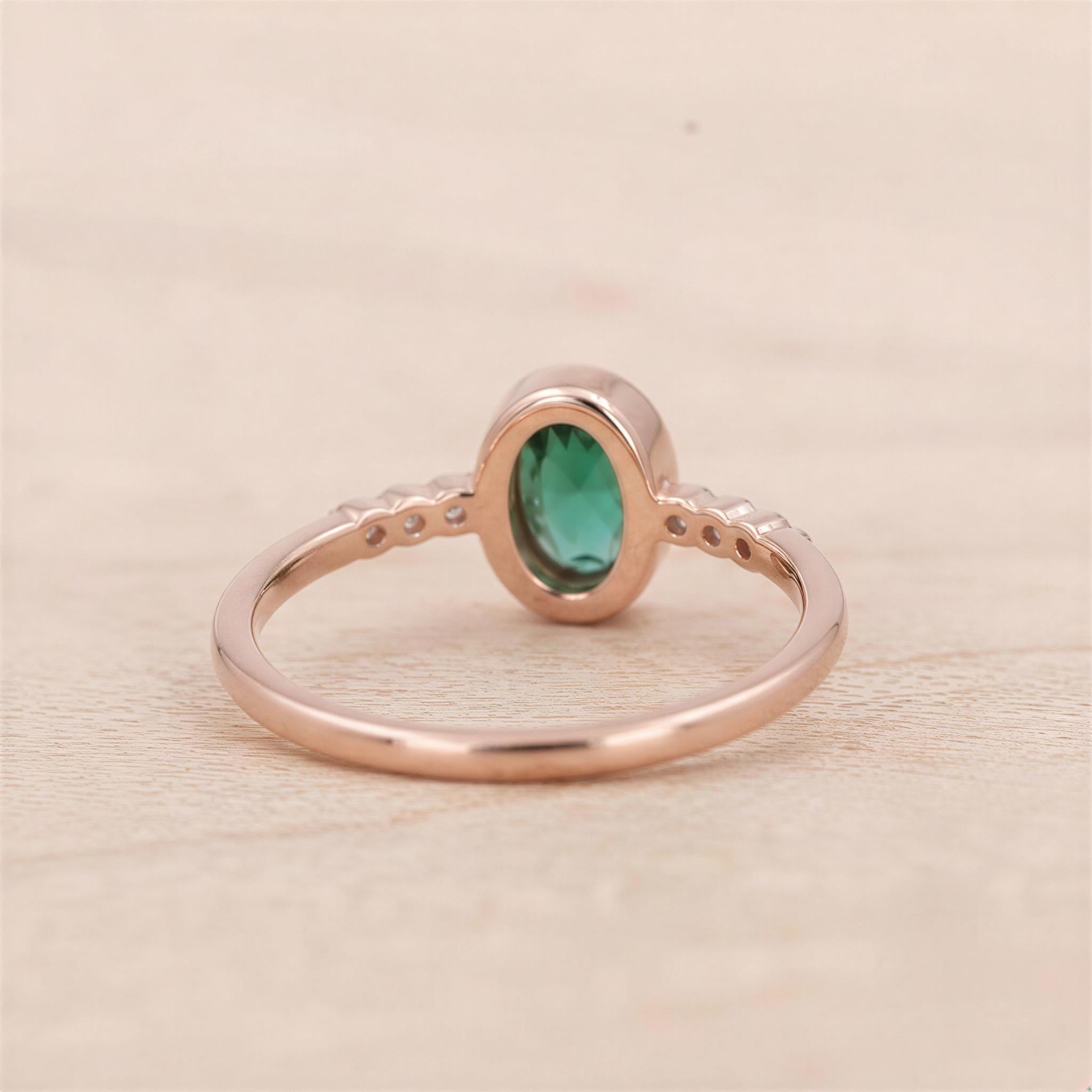 A rose gold ring with a large oval-shaped gemstone, likely an emerald, set in the center.
