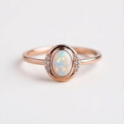 A rose gold ring with a large oval-shaped opal gemstone set in the center, surrounded by smaller diamonds.