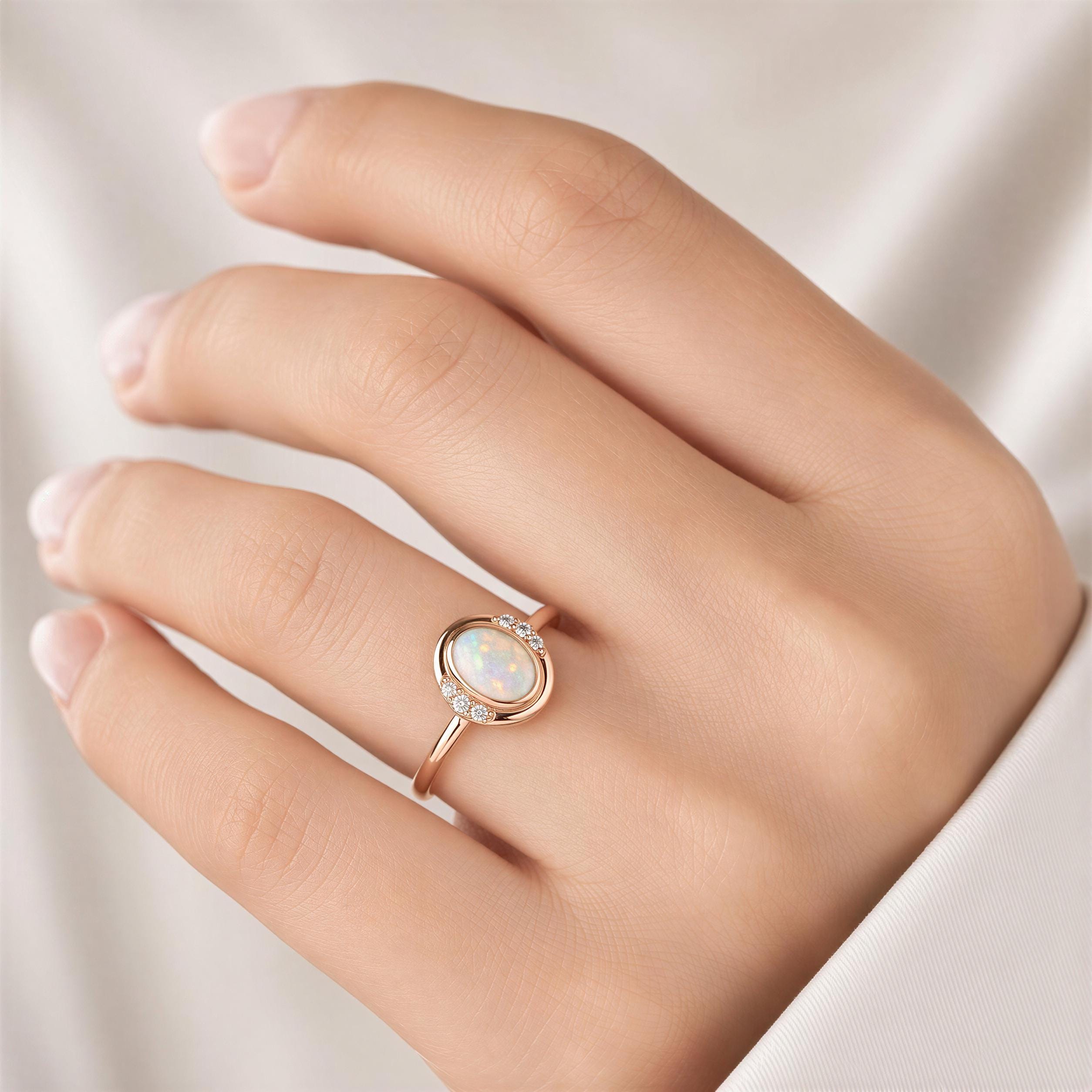 A close-up of a person's hand wearing a gold ring with a large oval-shaped opal stone.