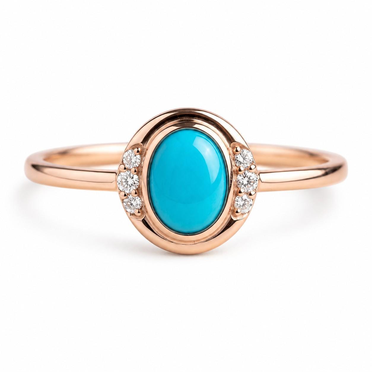 May include: A rose gold ring featuring a central oval-shaped turquoise cabochon stone. The setting is accented by three small round clear stones on each side of the turquoise, creating a symmetrical design on a smooth, polished rose gold band.