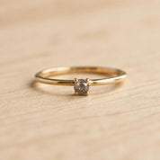 A simple gold ring with a small diamond set in the center, resting on a wooden surface.