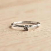 A simple silver ring with a small diamond set in the center, resting on a wooden surface.