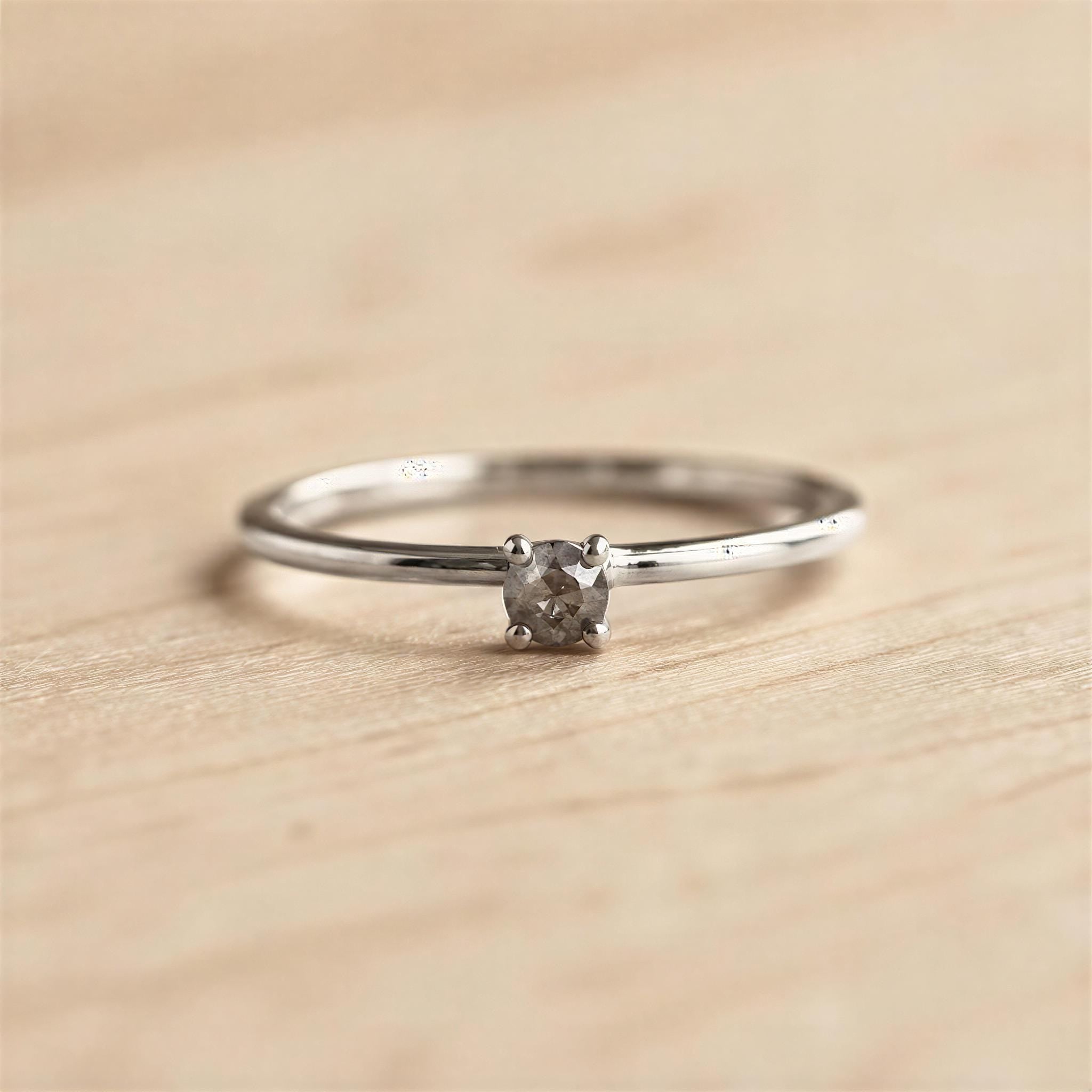 A simple silver ring with a small diamond set in the center, resting on a wooden surface.