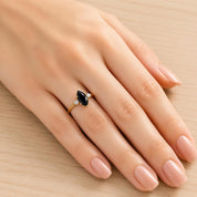 A close-up of a hand wearing a gold ring with a black gemstone.