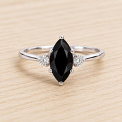 A silver ring with a large black gemstone, likely a diamond, as the centerpiece. The ring is set with smaller diamonds on either side of the large black gemstone.