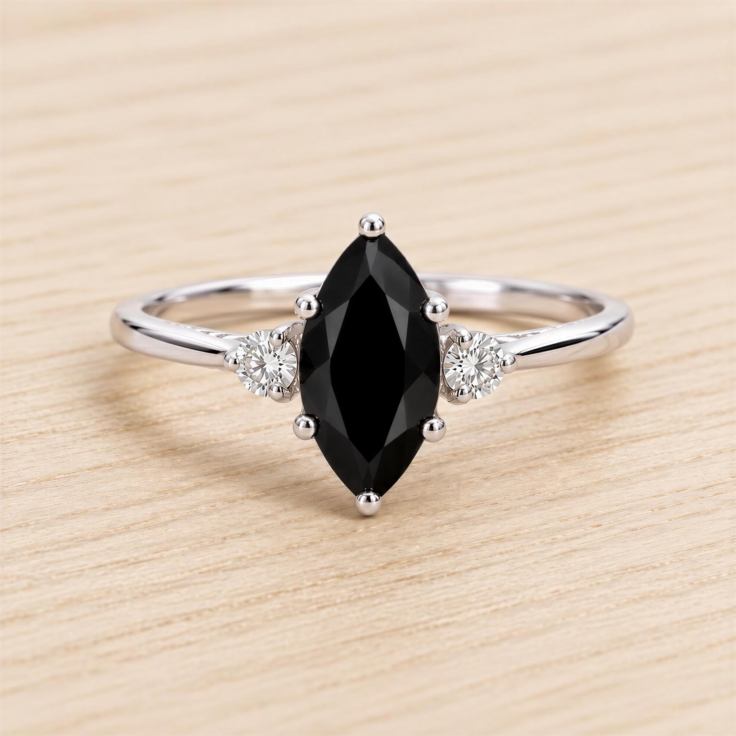 A silver ring with a large black gemstone, likely a diamond, as the centerpiece. The ring is set with smaller diamonds on either side of the large black gemstone.