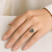 A close-up of a hand wearing a gold ring with a large gray gemstone.
