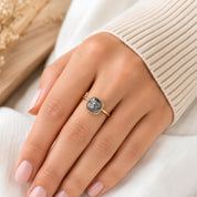 A close-up of a person's hand wearing a gold ring with a large, gray gemstone.