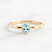 A gold ring with a blue gemstone, likely a blue topaz, set in the center.