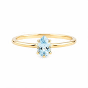 A gold ring with a single light blue gemstone, which appears to be a pear-shaped gemstone.