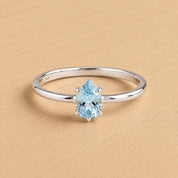 A silver ring with a blue gemstone, likely a diamond, set in the center.