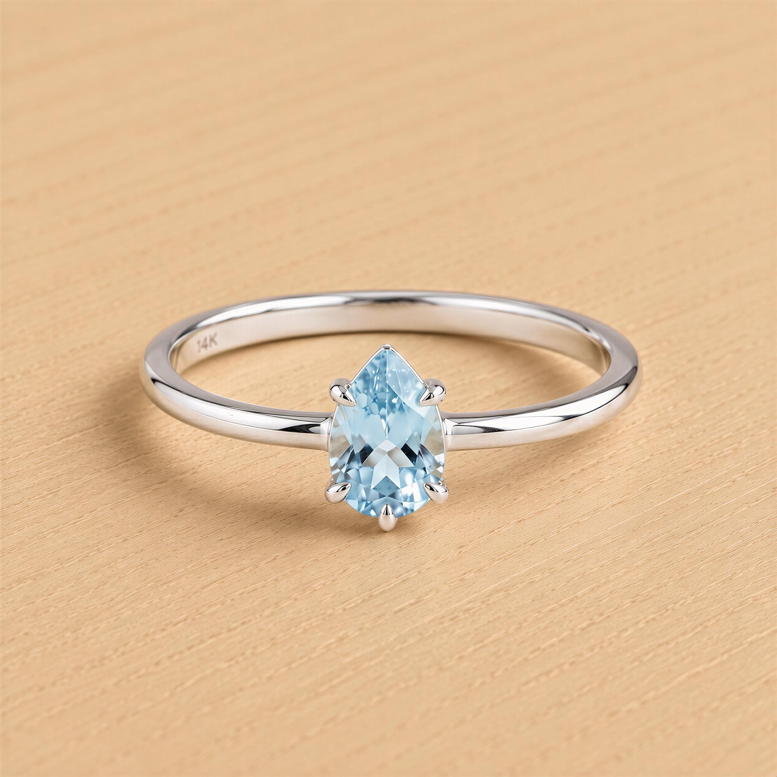 A silver ring with a blue gemstone, likely a diamond, set in the center.